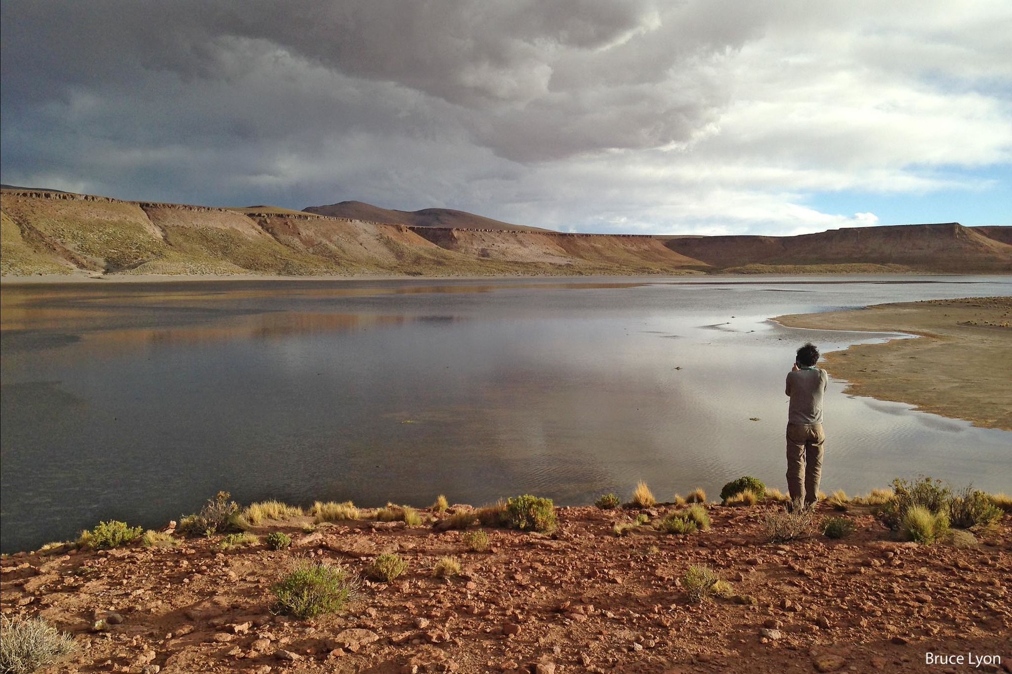 Una persona de espaldas mira una laguna de altura que refleja un cielo de tormenta.